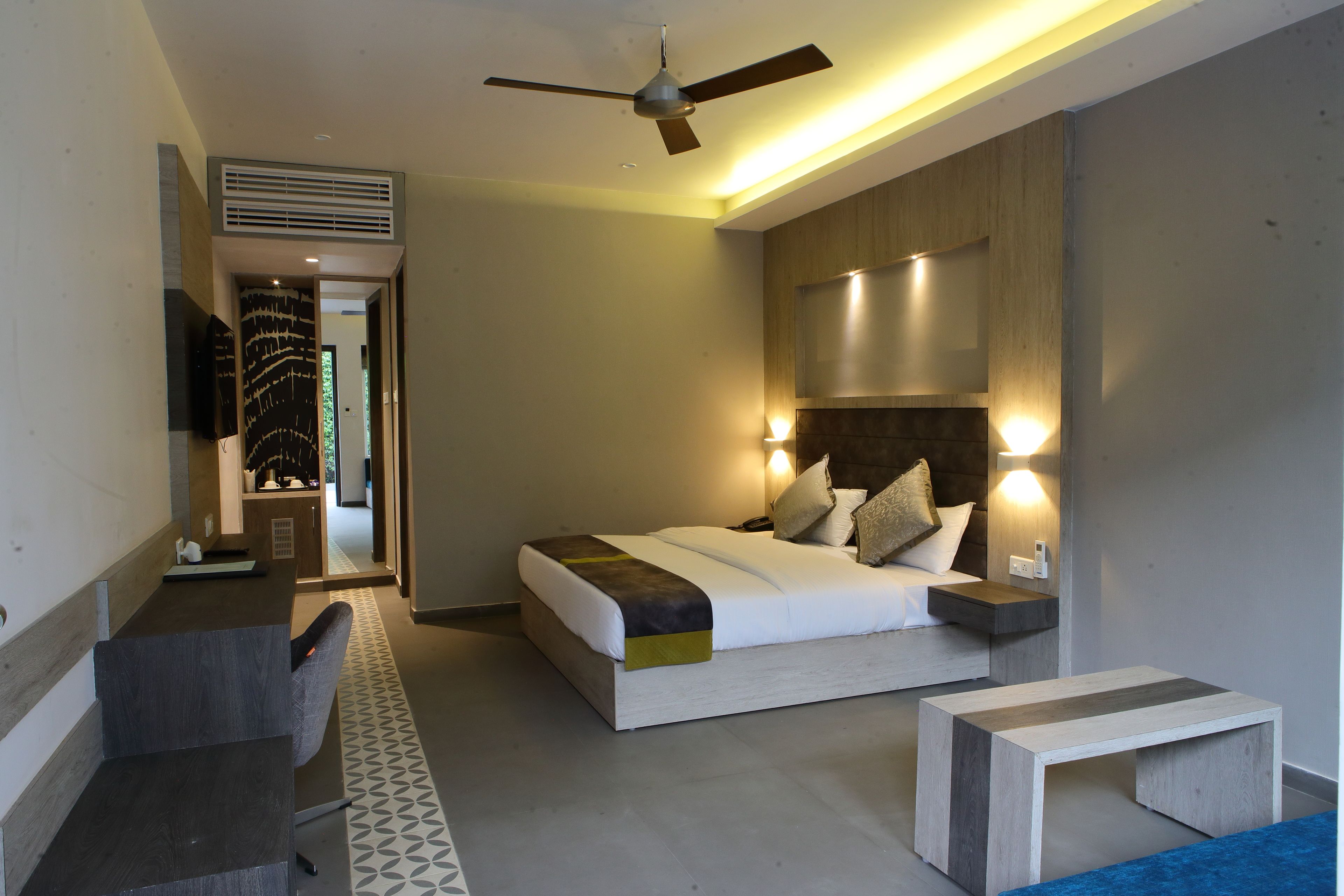 A modern hotel room with a bed, bedside tables, a desk, and a ceiling fan.