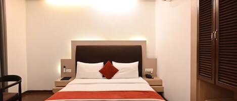 A hotel room with a bed, bedside tables, an air conditioning unit, and a wardrobe.