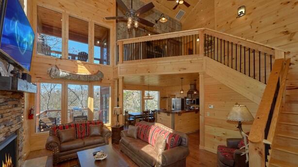 A spacious cabin with a large living area, a fireplace, a dining area, and a loft bedroom with a balcony. - Family Pool Cabin, Theater, Gameroom, Hot Tub (Gatlinburg)