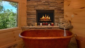 A stone fireplace with a fire, a stone shelf with candles and glasses, and a copper bathtub. - Family Pool Cabin, Theater, Gameroom, Hot Tub (Gatlinburg)