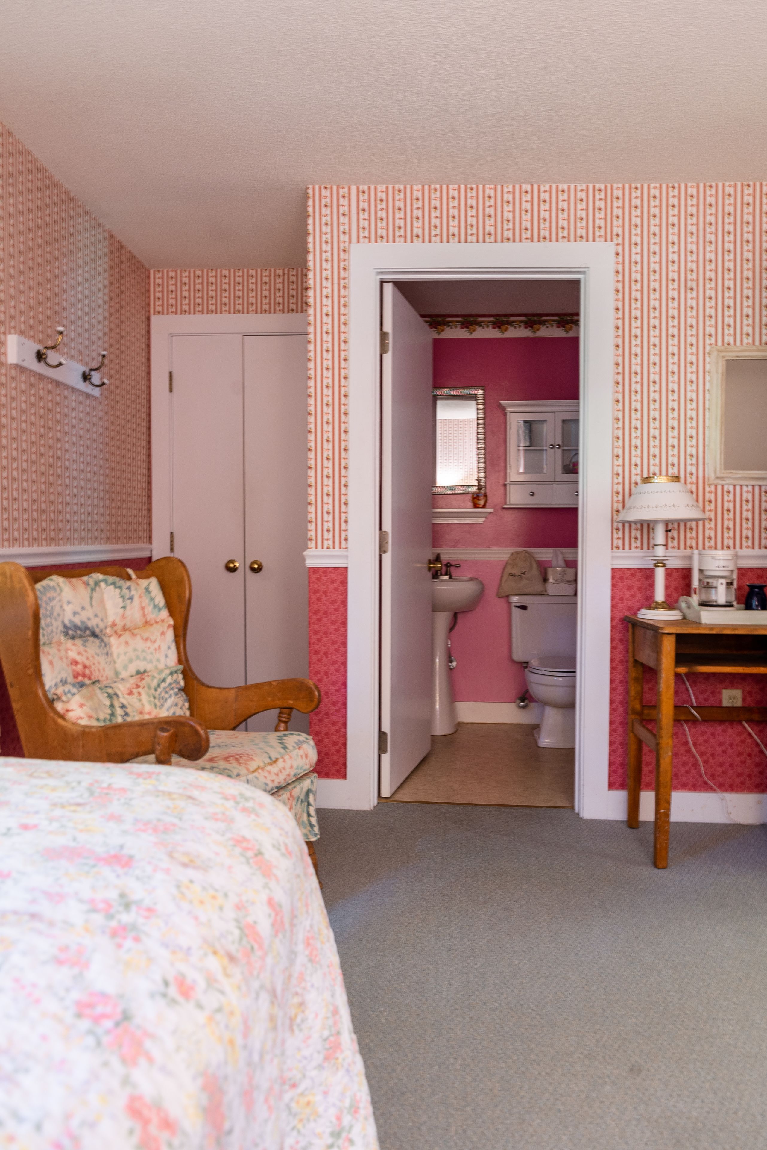 A bedroom with a bed, a chair, a desk, and a bathroom with a sink and toilet.