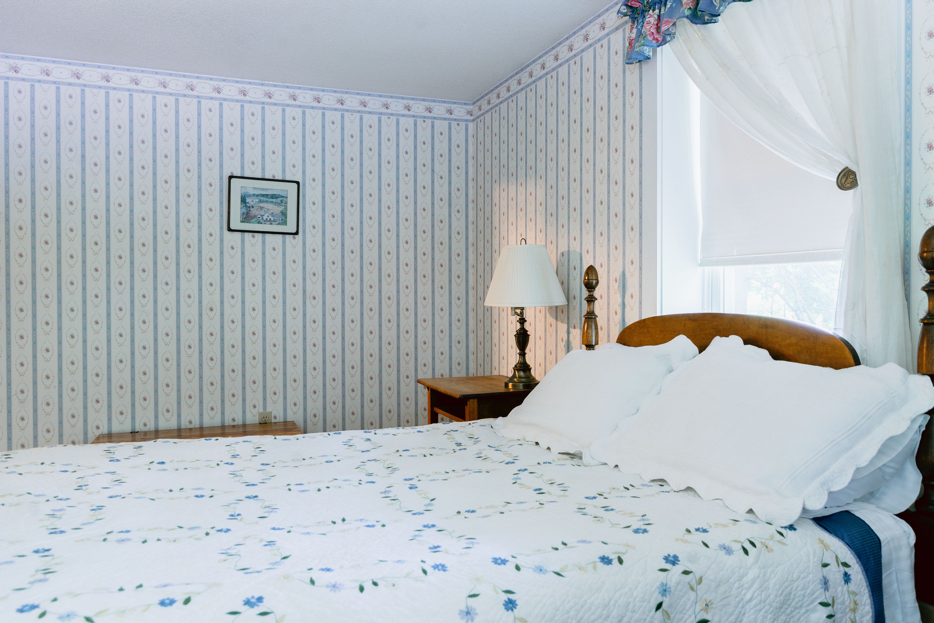 A bedroom with a bed, a nightstand, a lamp, and a window with curtains.