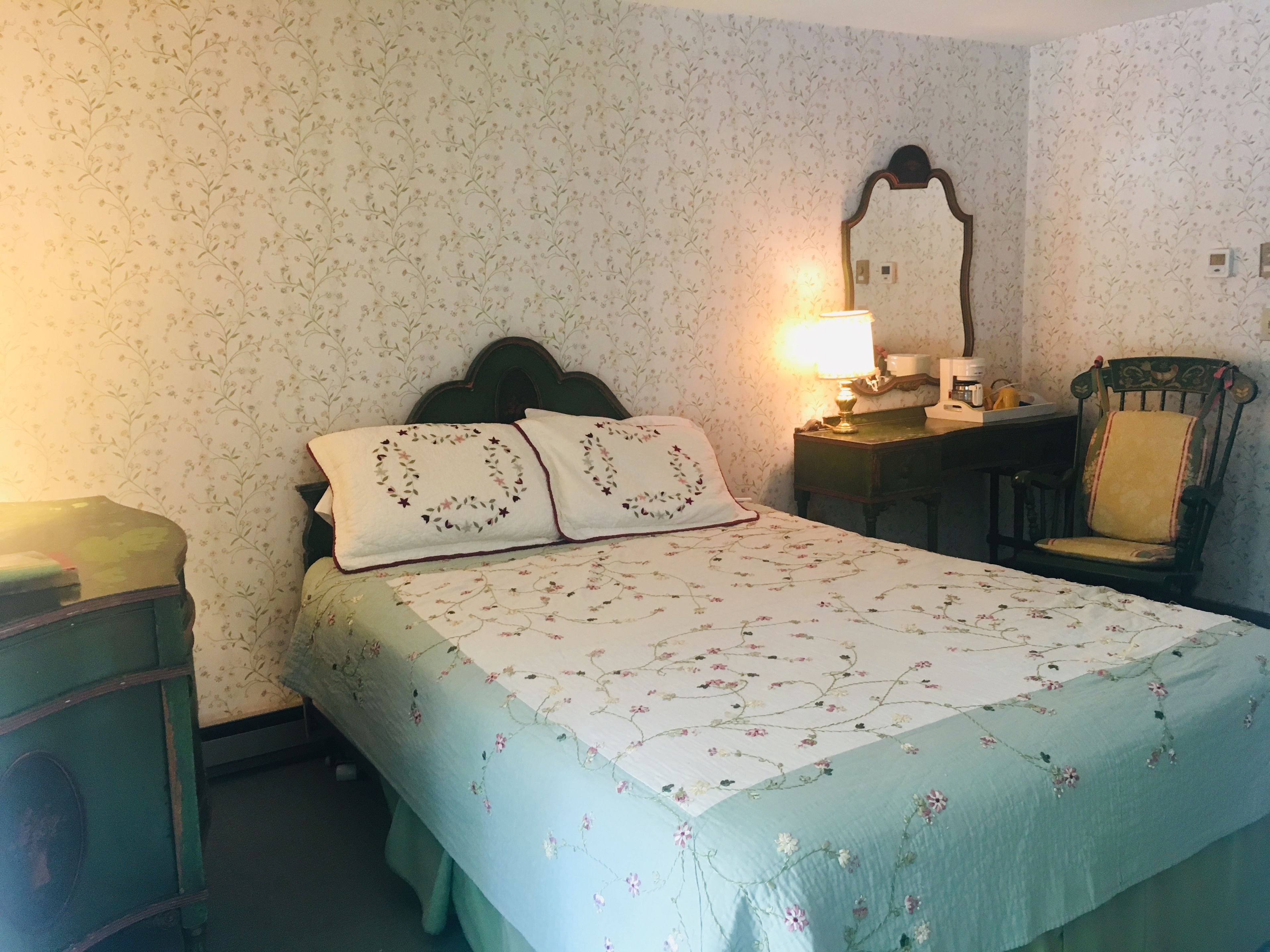 A bedroom with a bed, a nightstand, a chair, a lamp, and a mirror.