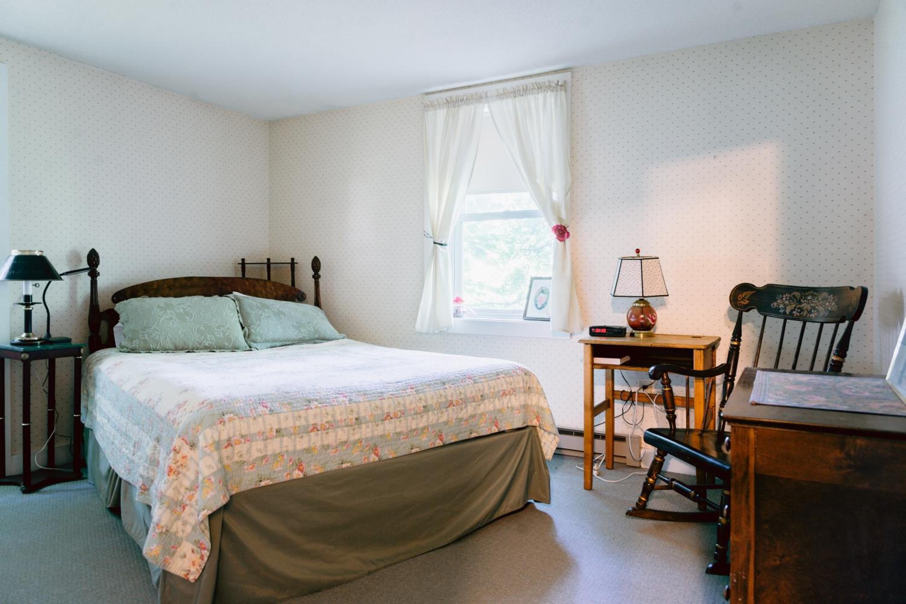 A bedroom with a bed, a desk, a chair, and a lamp.