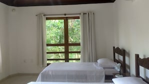 Ein Schlafzimmer mit zwei Betten, einem fensterbelaubten Fenster, einer Holzbalkendecke und einem Nachttisch mit Lampe.