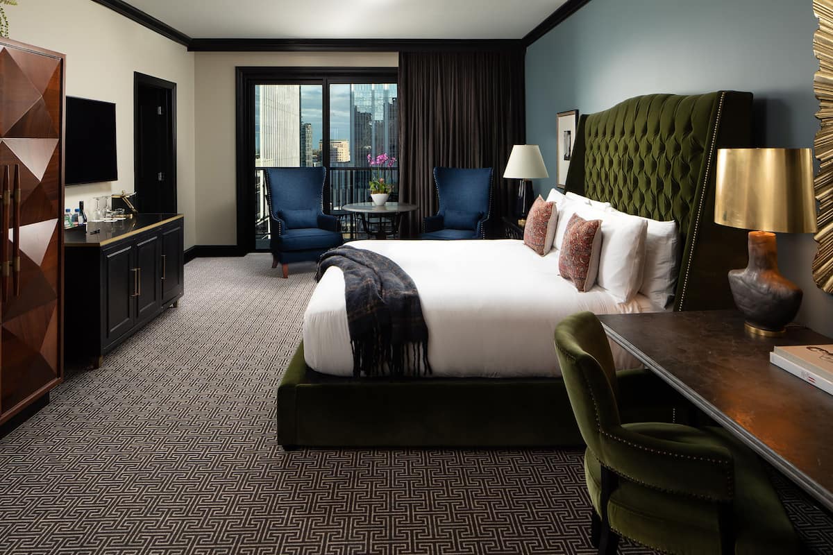 A hotel room with a large bed, two armchairs, a small table with a plant, and a desk with a lamp.