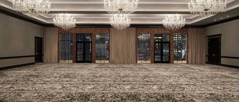 A large, carpeted room with chandeliers, large windows, and a brick wall.