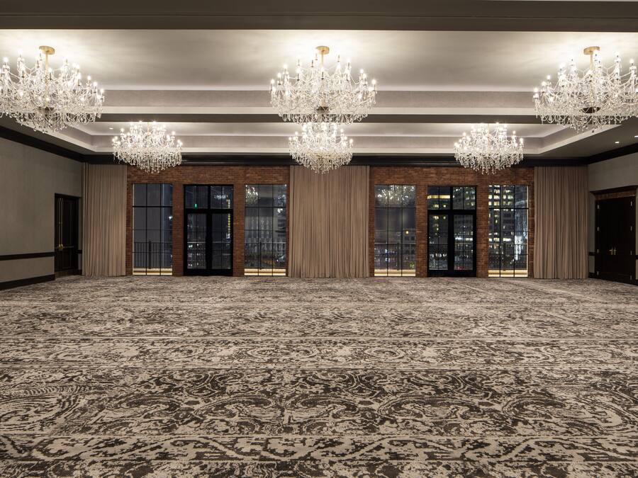 A large, carpeted room with chandeliers, large windows, and a brick wall.
