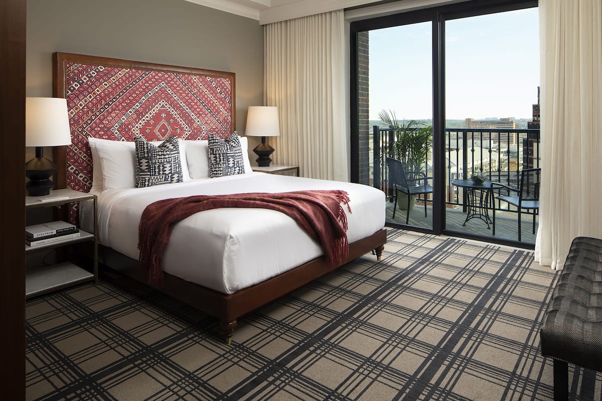 A hotel room with a large bed, two bedside tables with lamps, a patterned headboard, and a balcony with a view.