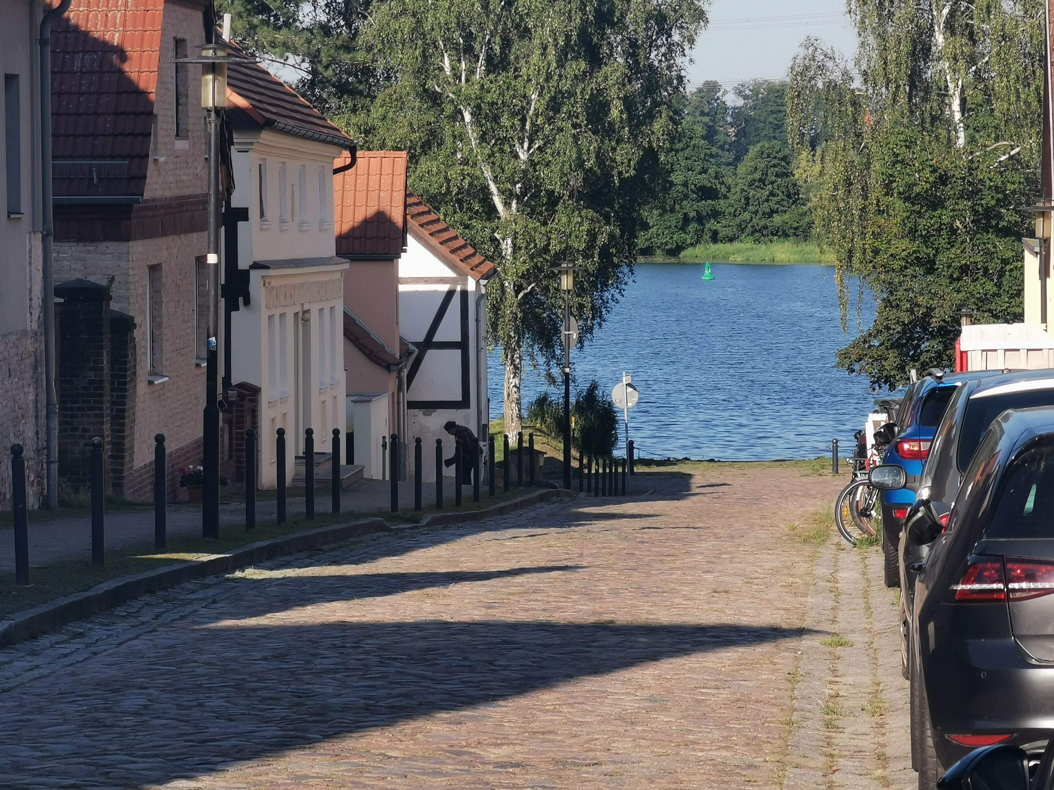 A cobblestone street with parked cars and a body of water in the background.