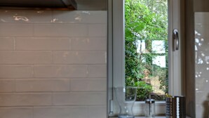 A kitchen with white tiled walls, a window with a view of greenery, and a glass door. - Vacation home in expansive nature with Wi-Fi - to Berlin  / Potsdam 35 minutes (Paretz an der Havel)