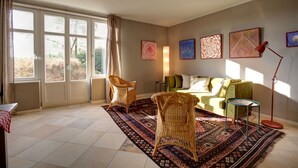 A living room with large windows, wicker chairs, a green sofa, and a patterned rug. - Vacation home in expansive nature with Wi-Fi - to Berlin  / Potsdam 35 minutes (Paretz an der Havel)
