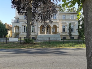 Un bâtiment de style classique, doté d’une façade symétrique, de grandes fenêtres et d’une entrée centrale avec des marches.