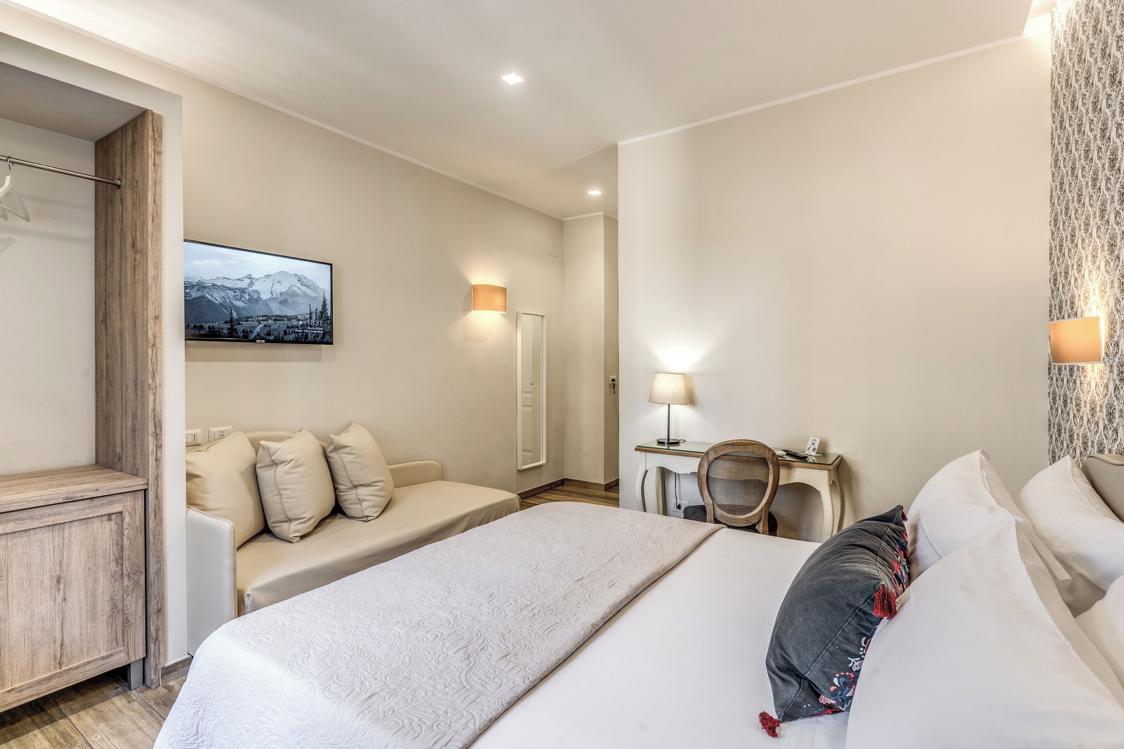 A hotel room with a bed, a desk, a chair, and a sofa.