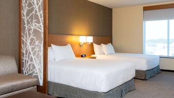 A hotel room with two beds, a sofa, a decorative wall panel, and a large window.