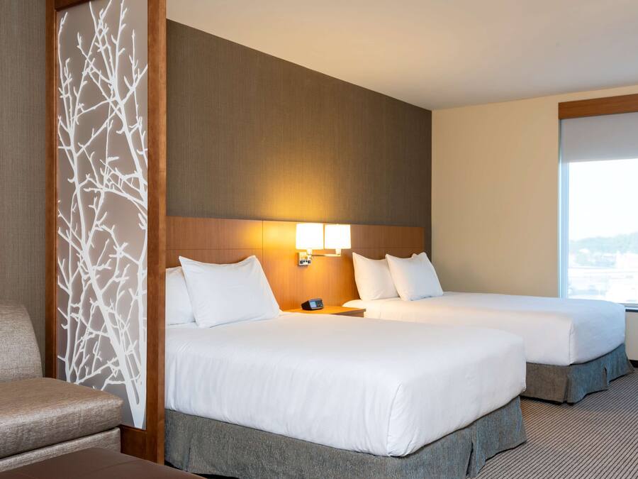 A hotel room with two beds, a sofa, a decorative wall panel, and a large window.