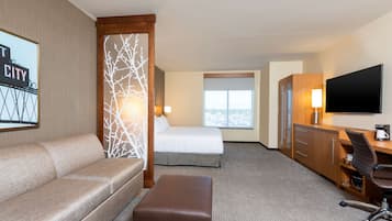 Habitación de hotel con cama, sofá, escritorio, televisión y ventana con vista a la ciudad.