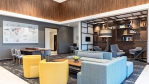 A modern hotel lobby with a wooden ceiling, a large map on the wall, a seating area with sofas and chairs, and a staircase with a lamp. - Hyatt Place Flint / Grand Blanc (Flint)