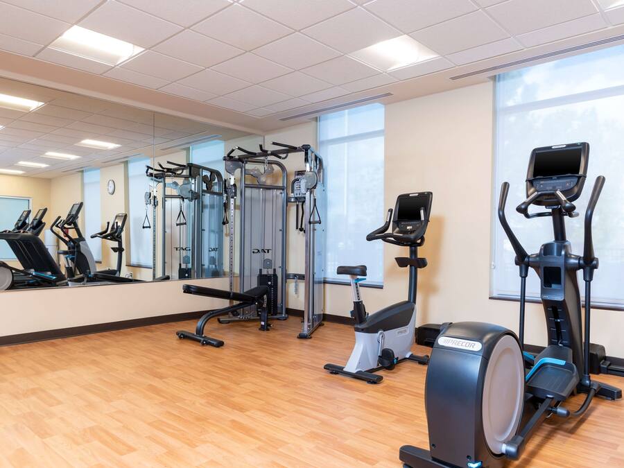 Een sportschool met diverse fitnessapparaten, grote ramen en een houten vloer.
