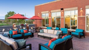 An outdoor patio with wicker furniture, red umbrellas, and a brick building in the background. - Hyatt Place Flint / Grand Blanc (Flint)