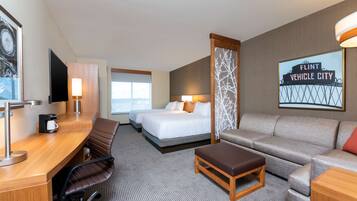 A hotel room with a desk, two beds, a sofa, a coffee maker, and a TV.