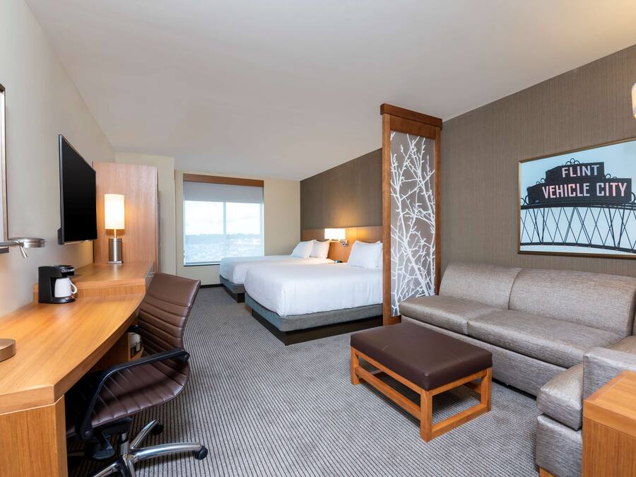 A hotel room with a desk, two beds, a sofa, a coffee maker, and a TV.