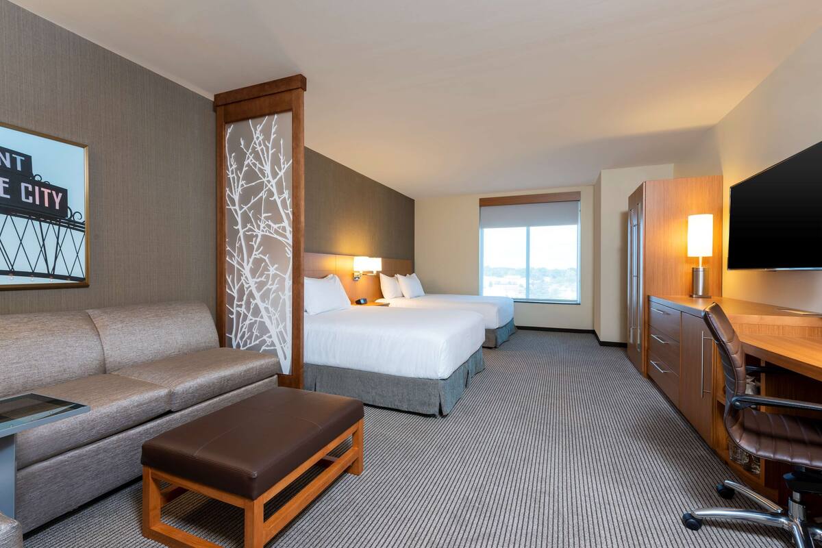 Habitación de hotel con sofá, dos camas, escritorio, televisor y ventana con vistas.