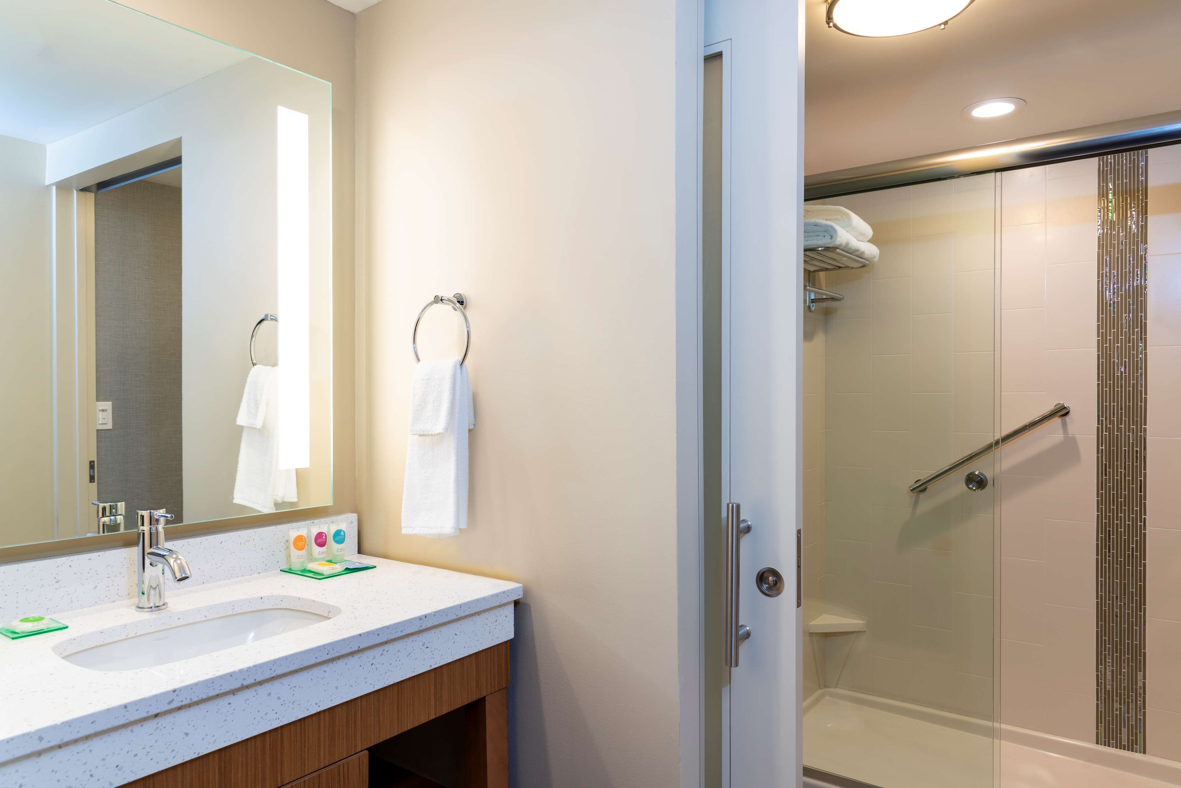 Un baño moderno con un espejo grande, dos lavamanos, cabina de ducha de vidrio y un perchero para toallas.