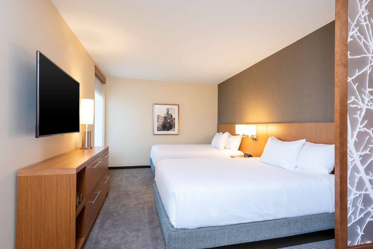 Habitación de hotel con dos camas, un televisor de pantalla plana, un aparador de madera y un cuadro enmarcado en la pared.
