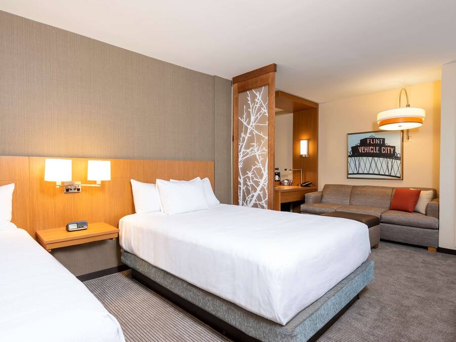 A hotel room with two beds, a sofa, a desk, and a mirror.