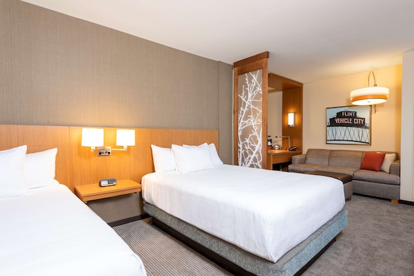 A hotel room with two beds, a sofa, a desk, and a mirror.