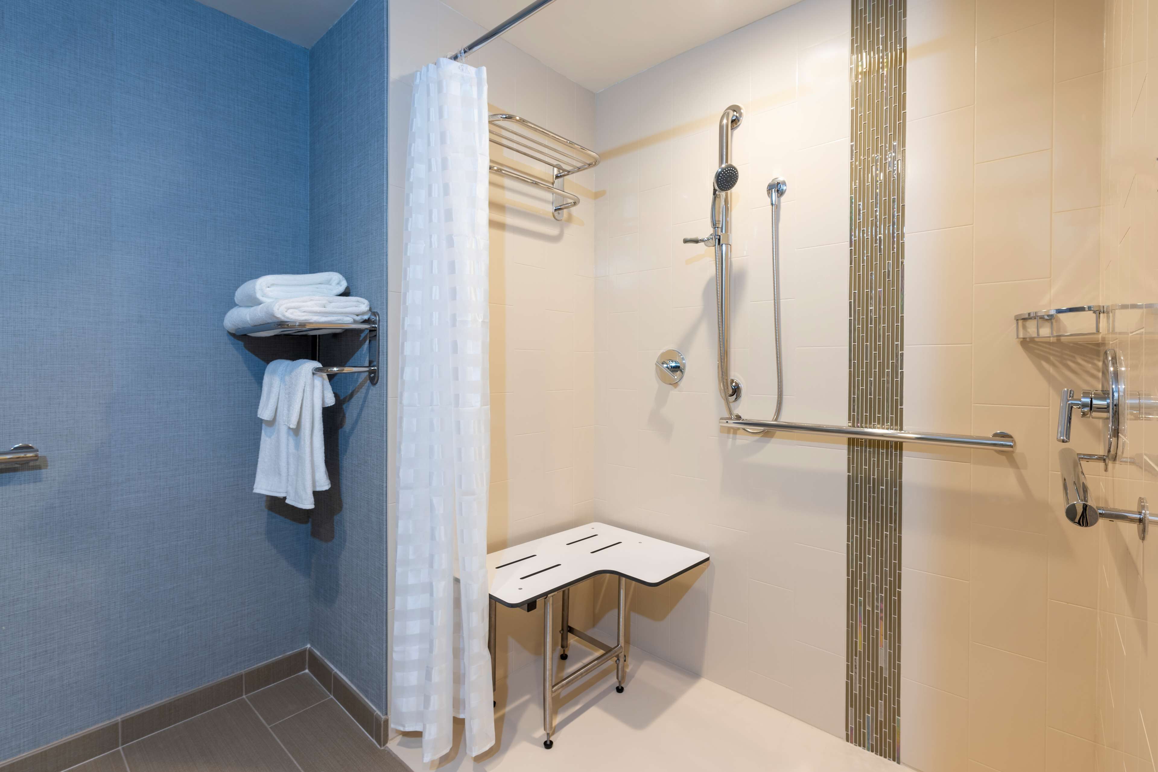 A shower area with a glass door, a towel rack with folded towels, and a small white table.