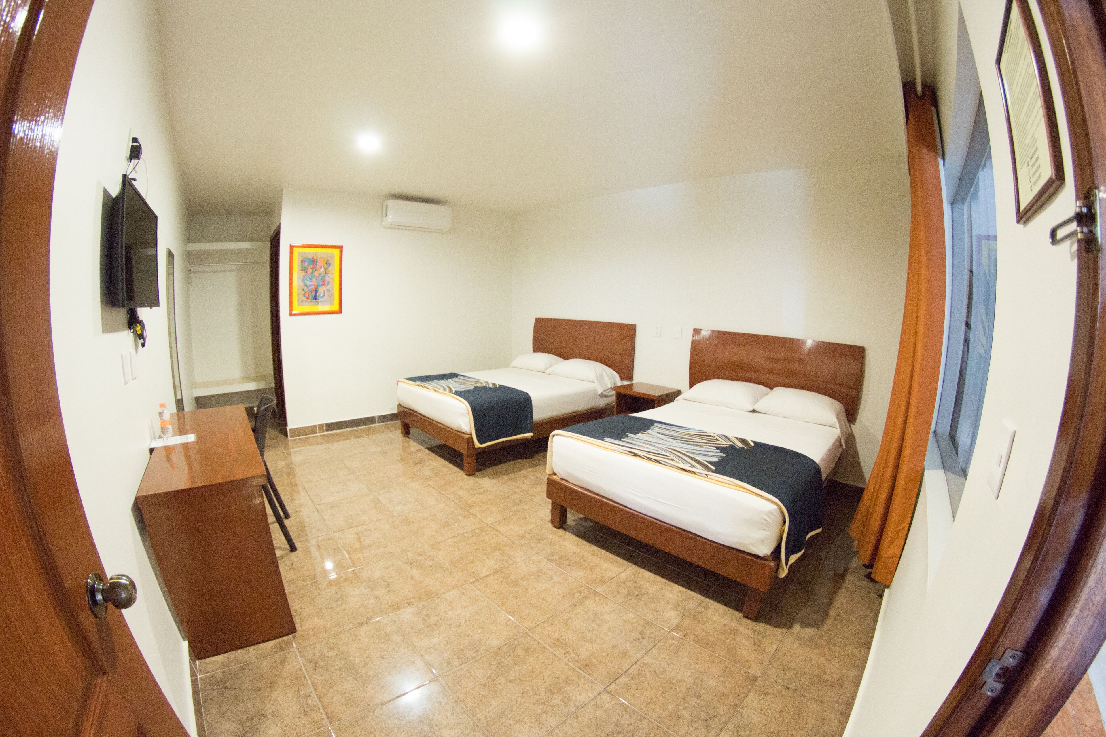A hotel room with two beds, a desk, and a television.