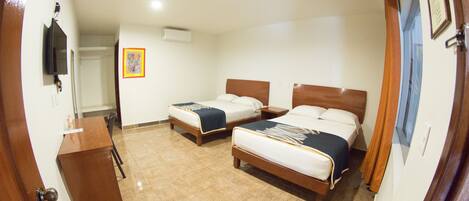 A hotel room with two beds, a desk, and a television.