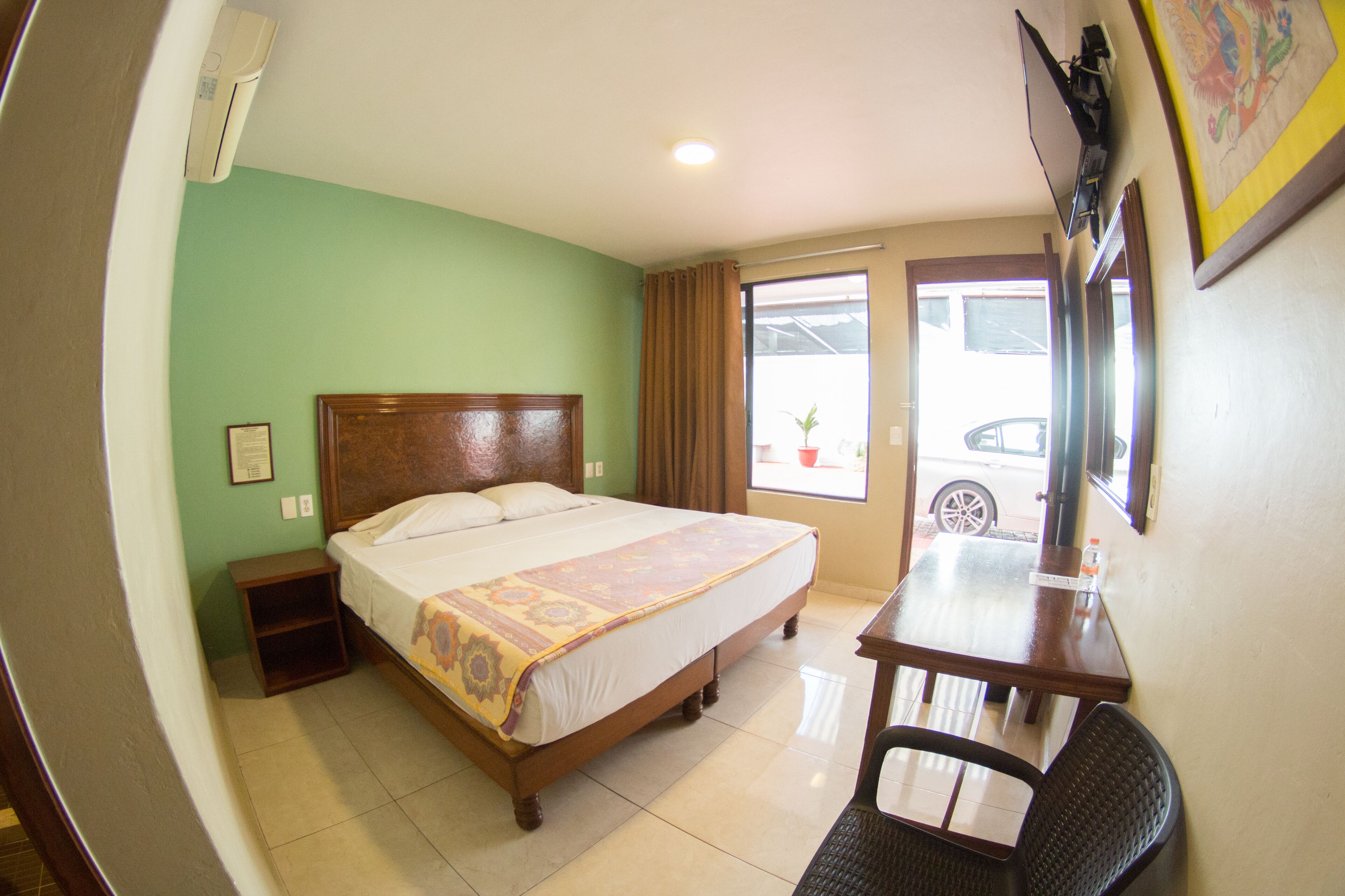 A hotel room with a bed, bedside table, chair, and a window with a view of the street.