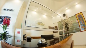 A hotel reception desk with a glass partition, a reception sign, a clock, and a floral arrangement. - Hotel Ricarlo (Iguala de la Independencia)