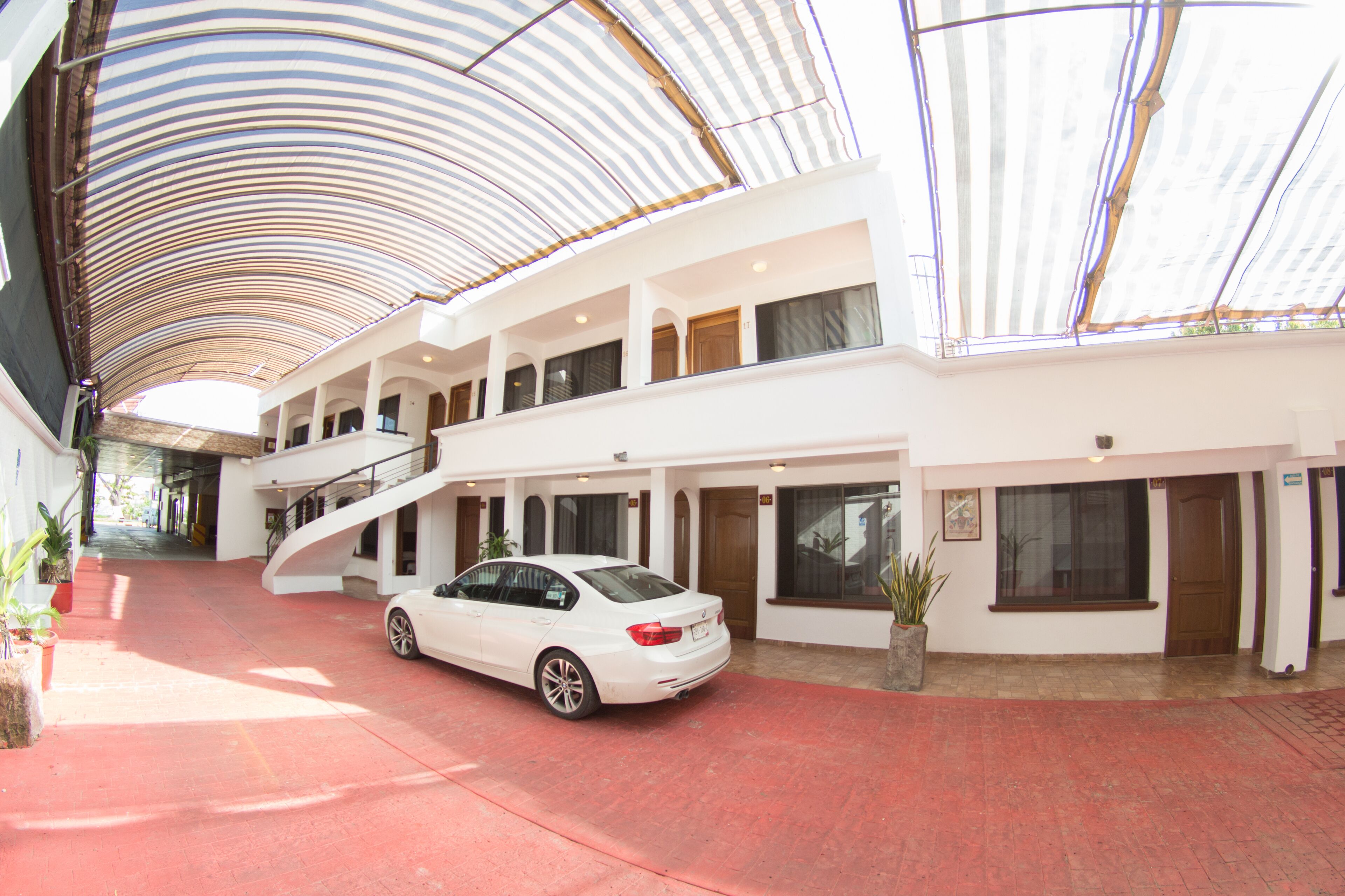 Un espai interior ample amb una cotxe blanc estacionat al centre, una escala que condueix a nivells superiors i una gran estructura de sostre corbada.