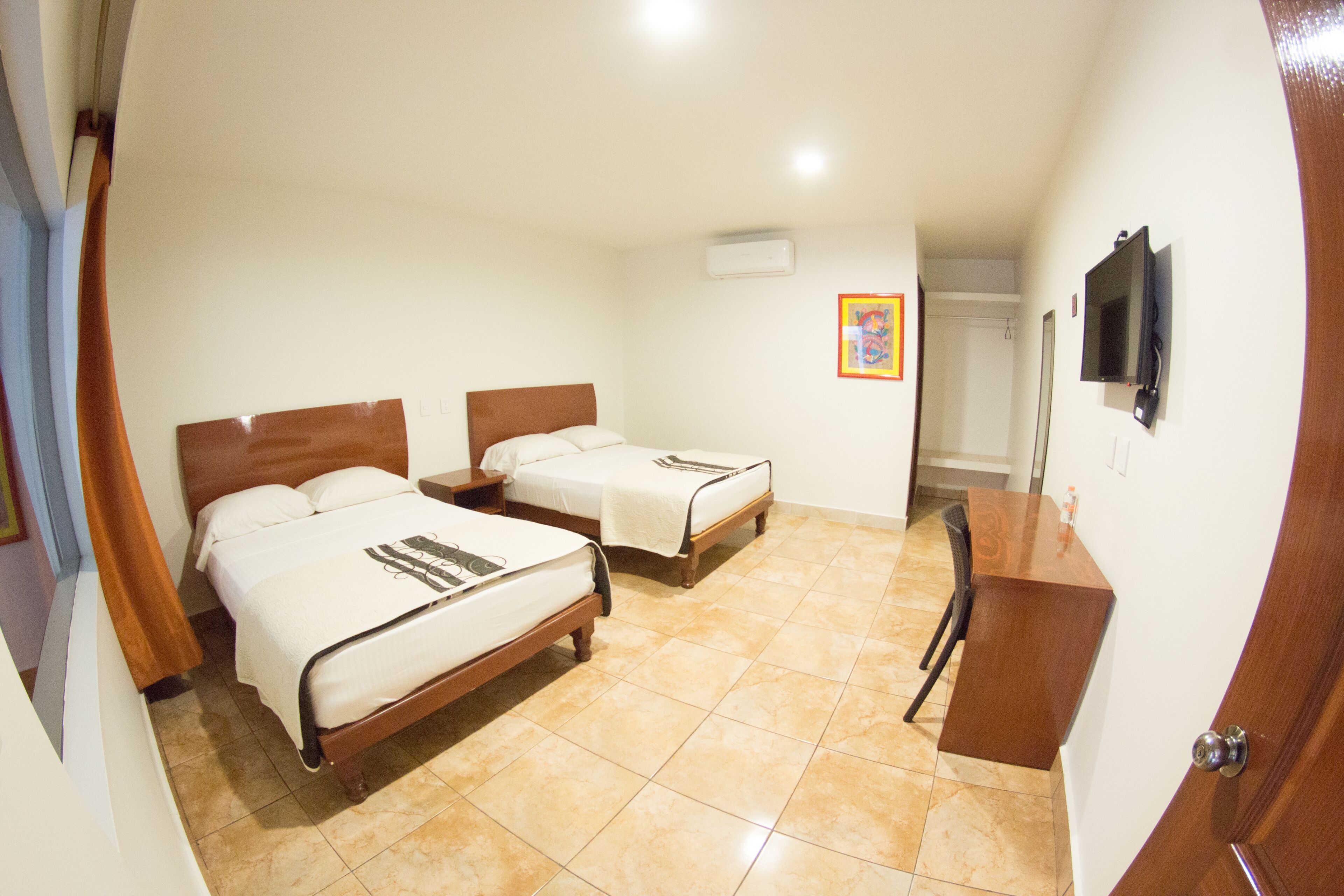 Habitación de hotel con dos camas, un escritorio, una silla y un televisor en la pared.
