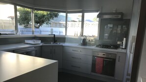 Une cuisine moderne dotée d’un grand îlot central, d’appareils électroménagers en acier inoxydable et offrant une vue sur le jardin arrière.