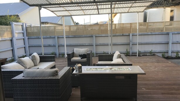 Une terrasse extérieure couverte, aménagée avec des meubles en osier et une table à plateau en verre.