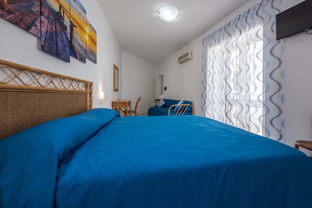 A bedroom with a large bed, a small table, a chair, and a sofa.