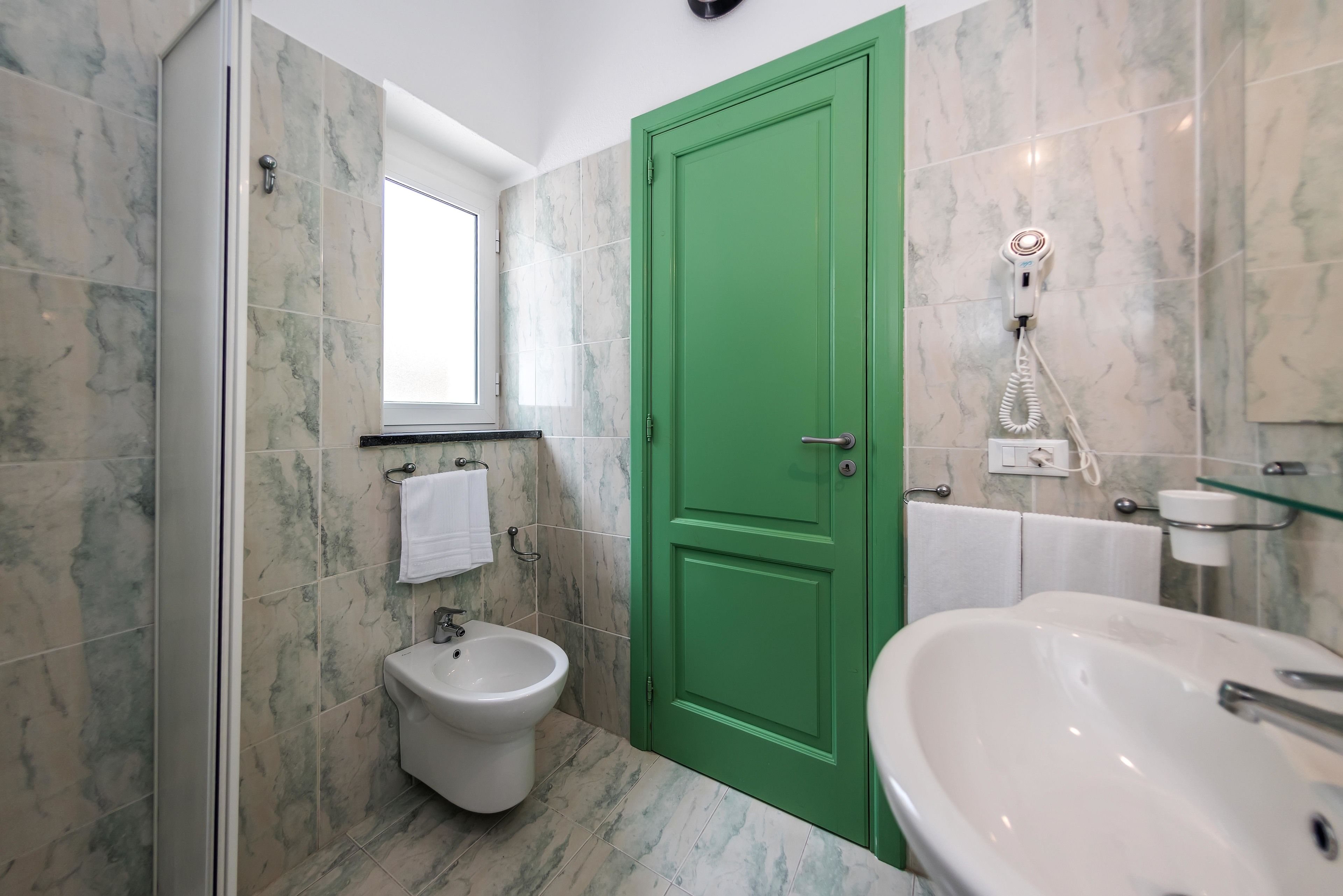 Une salle de bain avec une porte verte, un bidet, un grand lavabo et des carreaux de marbre.