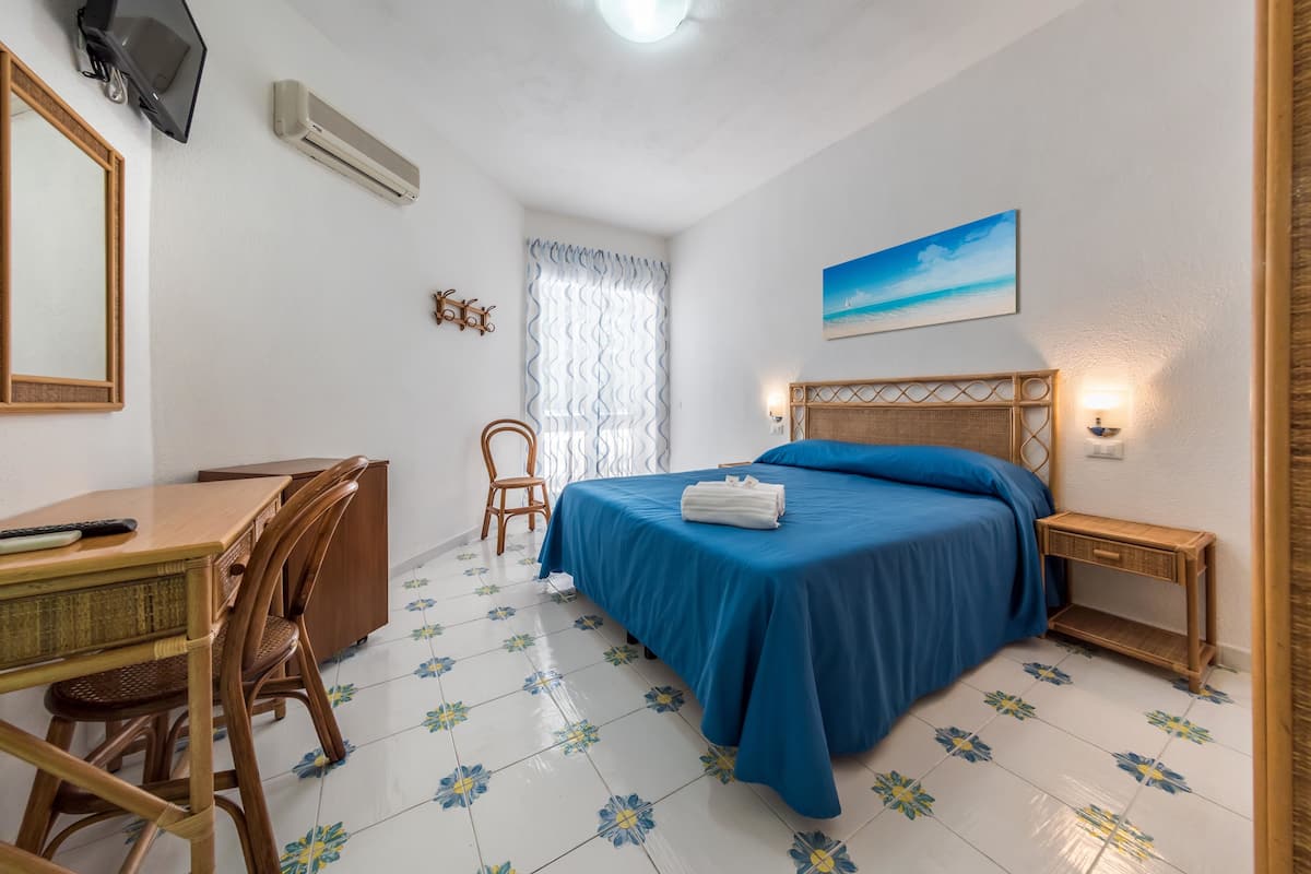 A bedroom with a bed, a desk, a chair, a TV, and a window with curtains.