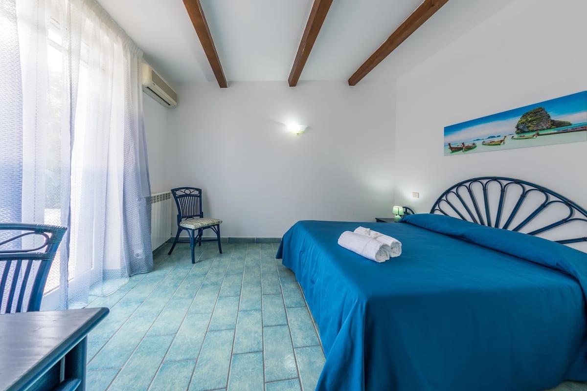 A room with a bed, a chair, a table, and a painting on the wall.