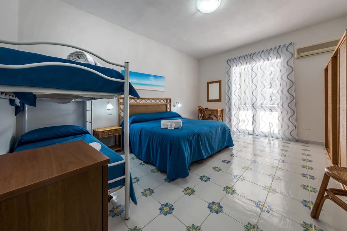 A room with a bunk bed, a desk, a chair, and a bed with a blue bedspread.