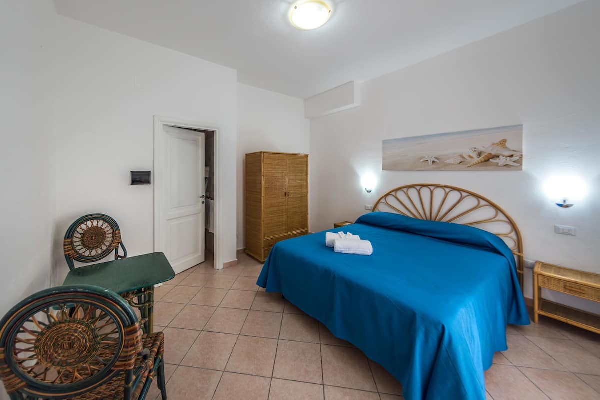 A bedroom with a bed, a wooden wardrobe, a chair, and a wall-mounted light fixture.