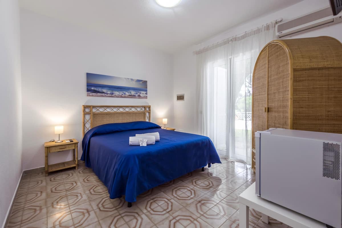 A hotel room with a bed, a nightstand, a wall-mounted air conditioner, and a window with curtains.