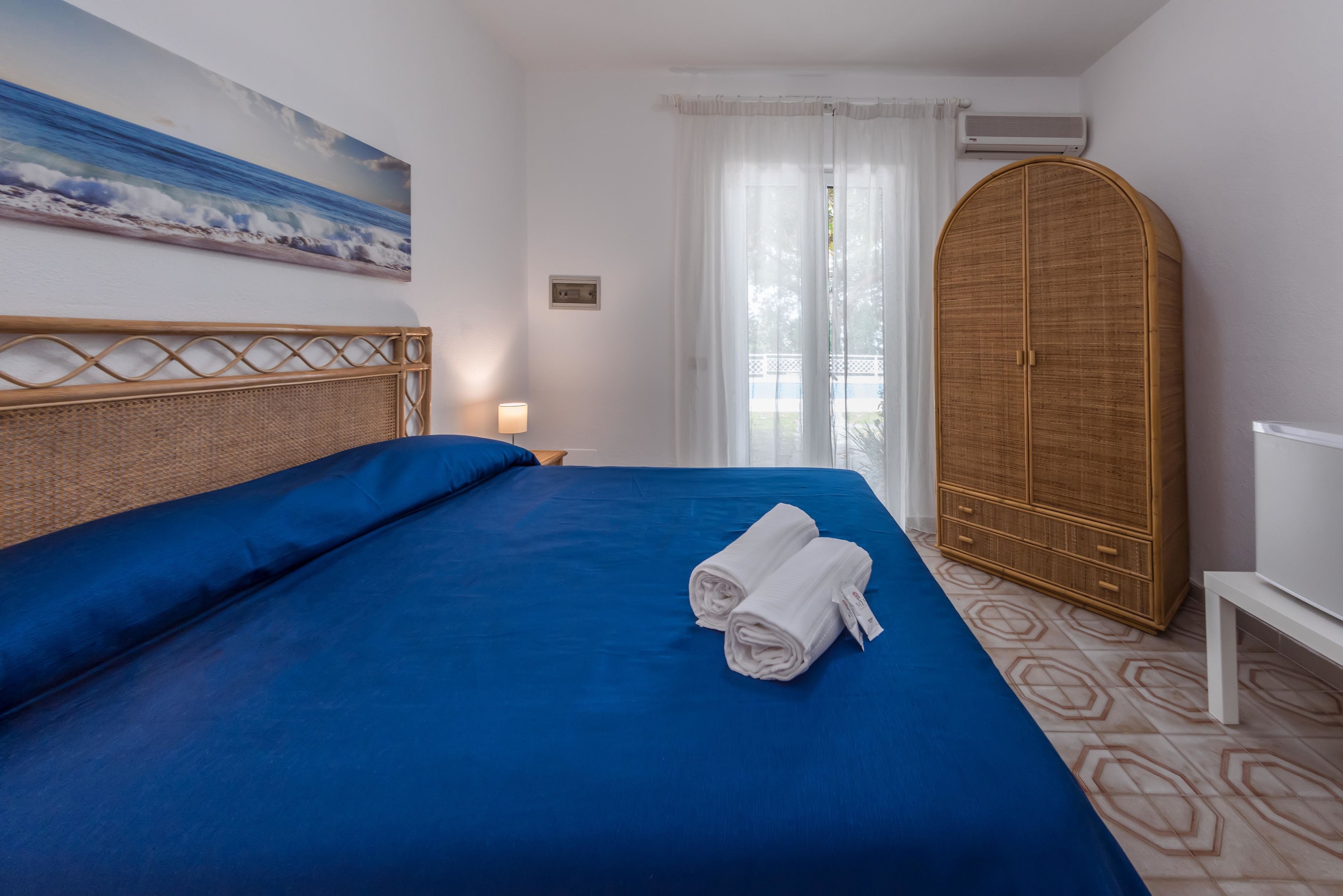 A hotel room with a large bed, a wooden wardrobe, and a painting of the ocean on the wall.