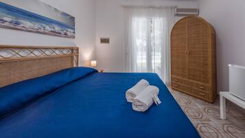 A hotel room with a large bed, a wooden wardrobe, and a painting of the ocean on the wall.