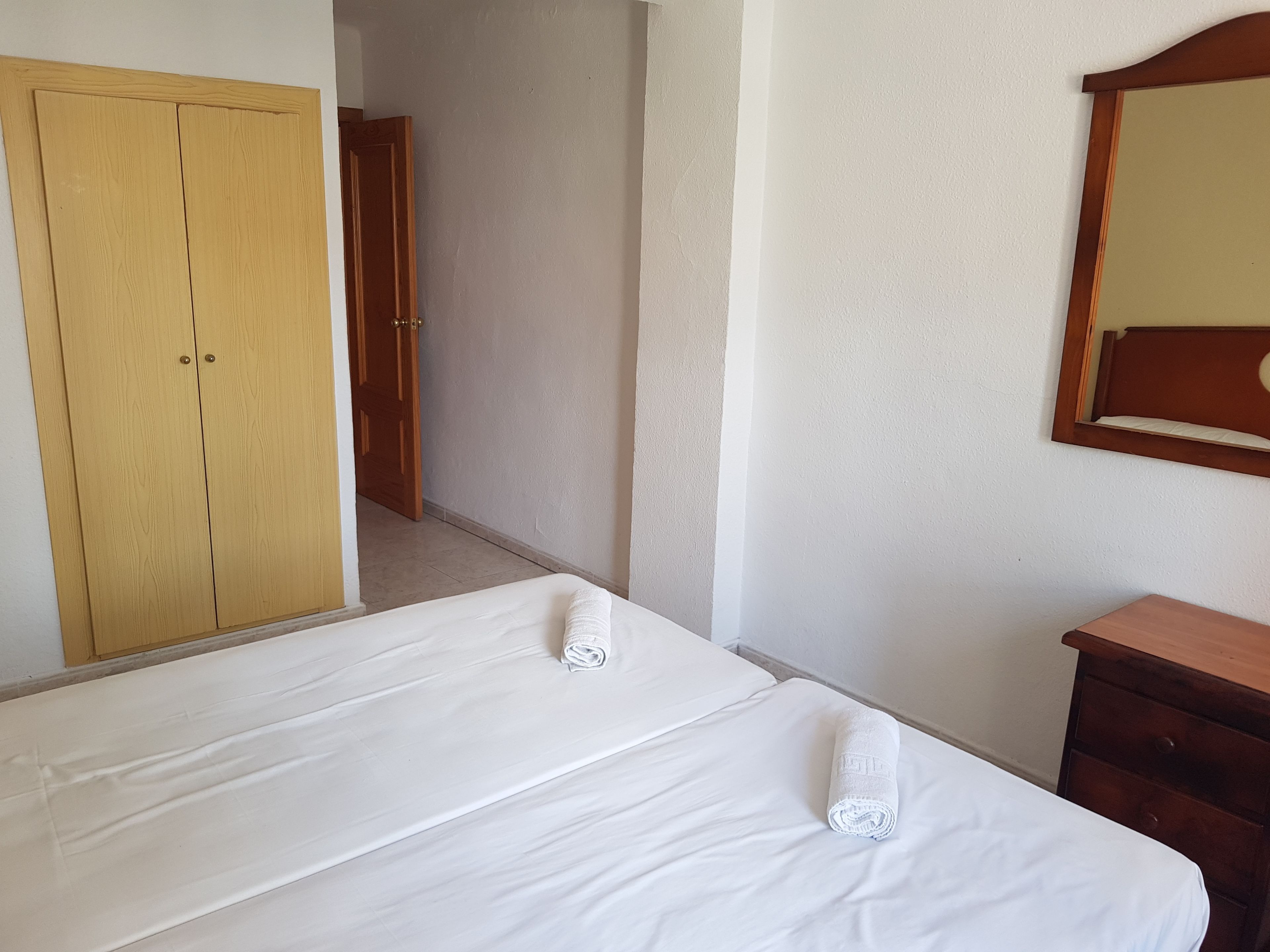 Habitació d'hotel amb un llit doble, un armari de fusta, una petita estanteria de fusta i un mirall a la paret.